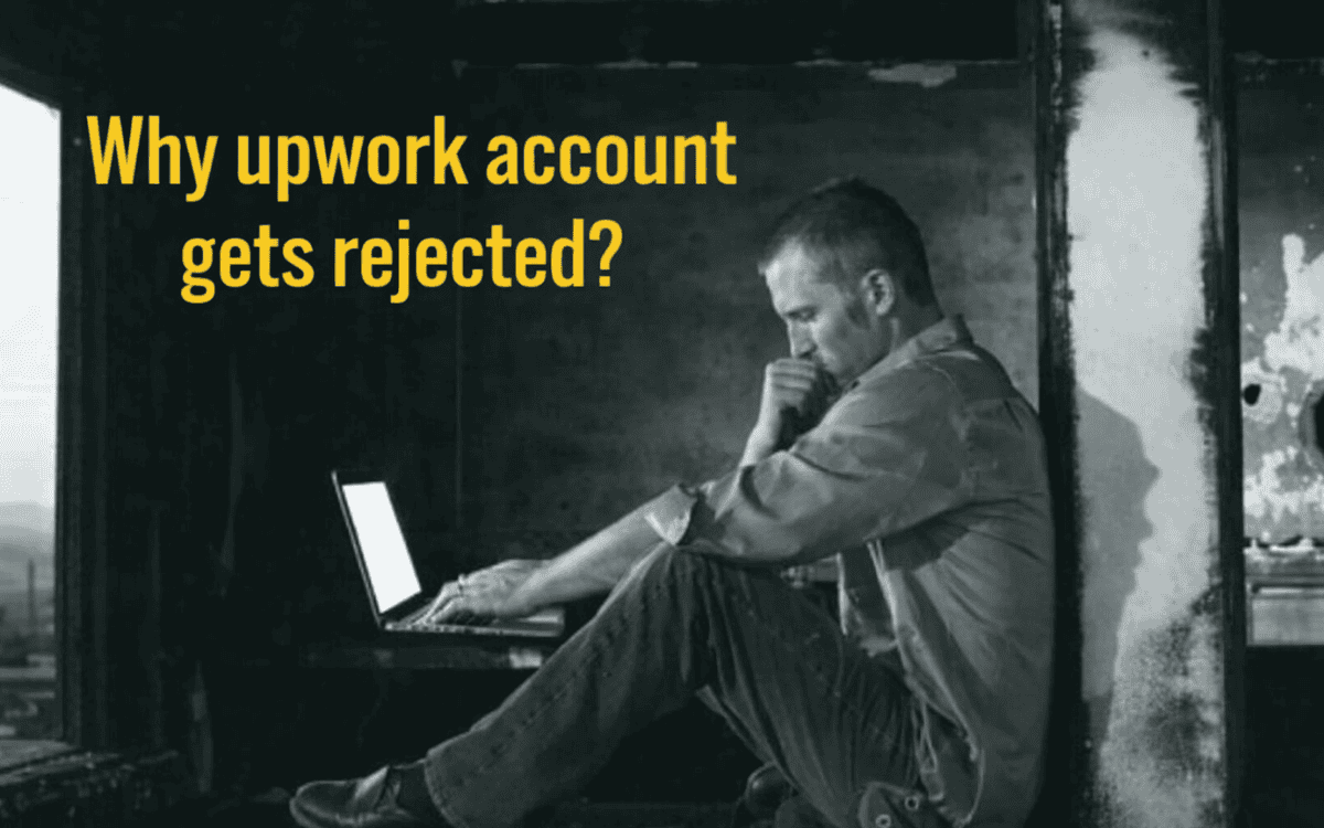 Man sitting on floor looking frustrated at open laptop with "Why Upwork account gets rejected?" text overlay in dark setting