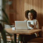 Woman using phone and laptop in cozy wooden room with soft lighting and relaxed setting